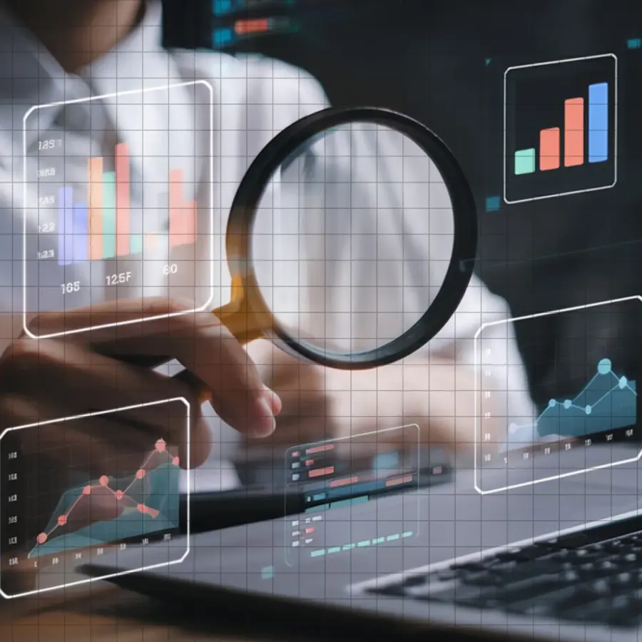 A magnifying glass held over charts and graphs floating above a laptop