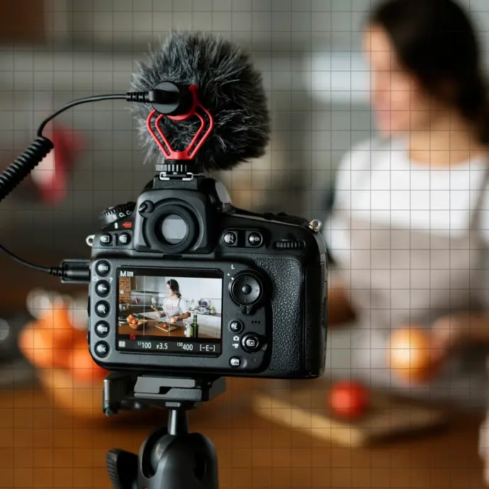 A camera on a tripod with a shotgun microphone filming a woman preparing food